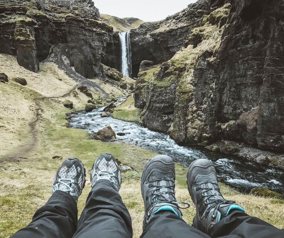 Picture of Jeannie and Husband Showing their Hiking Boots (as part of their Rain Gear for Iceland) Close to the Kvernufoss Waterfalll | Iceland with a View 