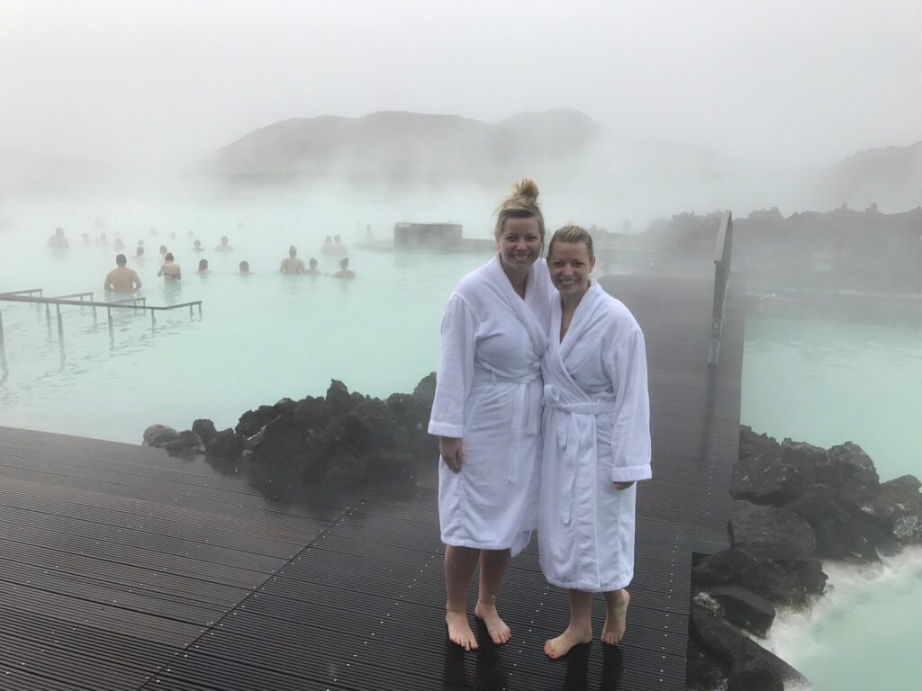 Picture of Jeannie and her friend standing in front of the Blue Lagoon with bath robes as part of the rule to shower before entering the pool | Blue Lagoon Iceland | Iceland with a View 