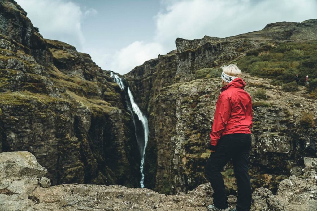 View Of The Glymur Waterfall Hike | Jeannie Wearing Red Jacket Staring Up At The Glymur Falls
