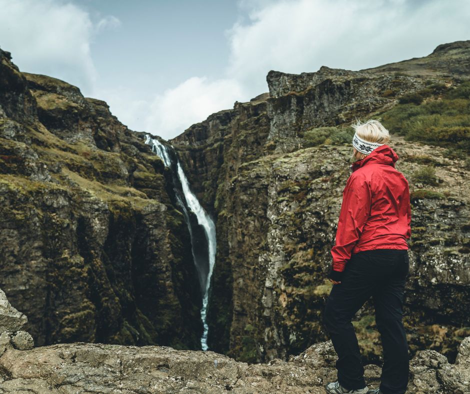 Picture of Jeannie Wearing a Red Raincoat Standing in Front of the Glymur Waterfall | Reykjadalur Hot Springs | Iceland with a View 