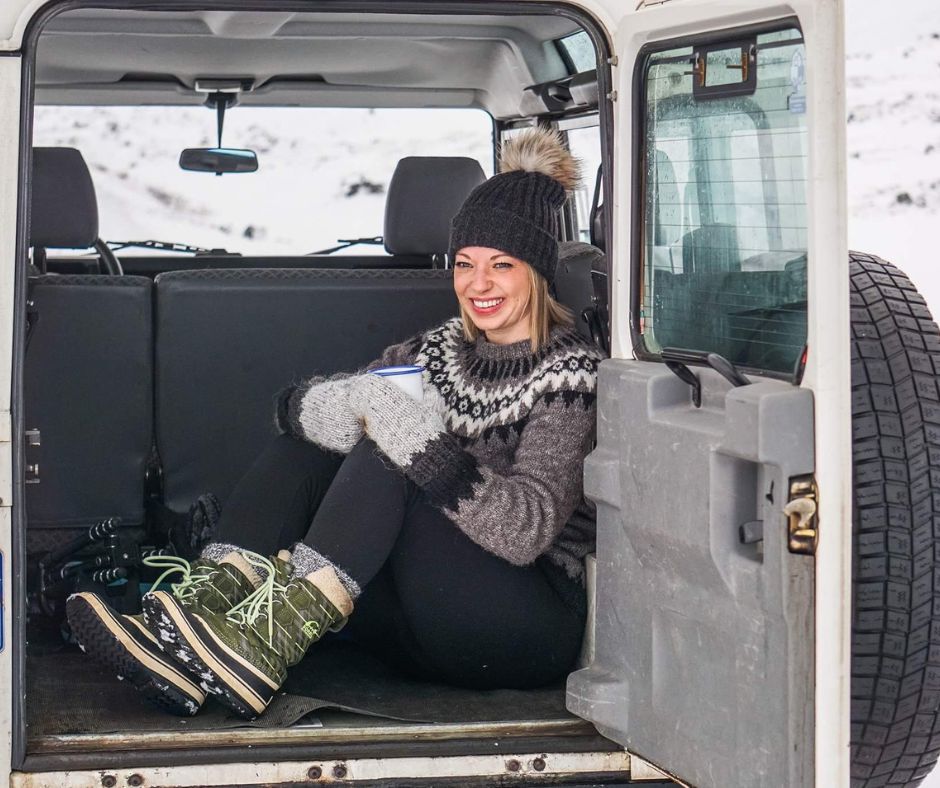 Picture of Jeannie in the Trunk of the Car while Sipping a Hot Drink Wearing Layers, Gloves, Hat, Lopapeysa (Icelandic Wool Sweater and Boots | Packing For A February Trip To Iceland  | Iceland with a View 