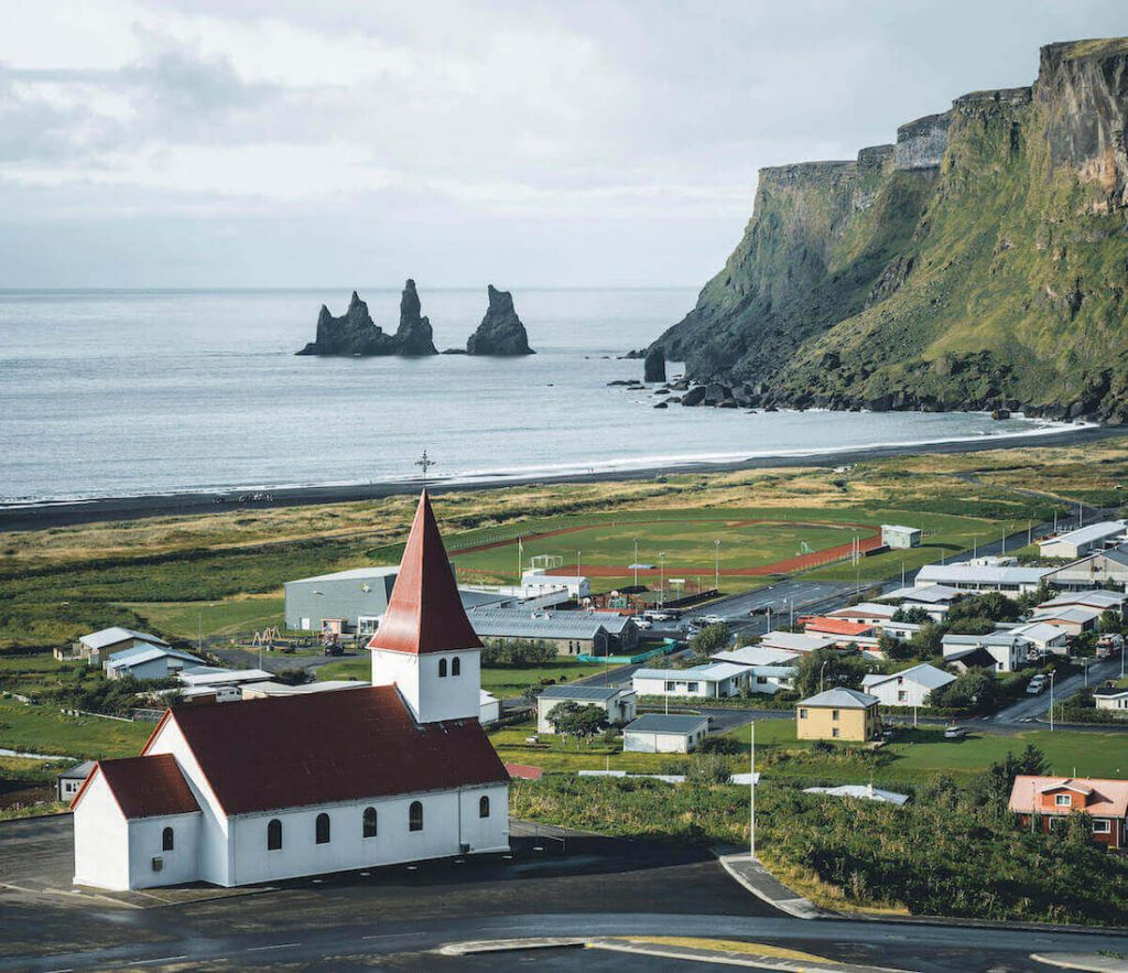 Picture of the iconic Vík í Mýrdal church with its distinctive red roof comes into view, perched at the top of the hill. | Vik, Iceland | Iceland with a View