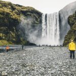 Picture of Jeannie Wearing a Yellow Raincoat Looking at the Skogafoss Waterfall in Iceland | Iceland Spring Packing | Iceland with a View