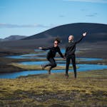 Two friends jump with joy in a stunning Icelandic mountain landscape.