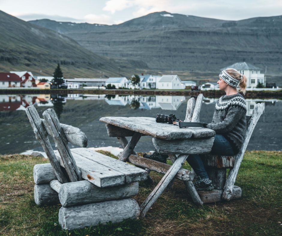 Picture of Jeannie Sitting on a Picnic Table with her Camera in Seydisfjordur | Iceland with a View