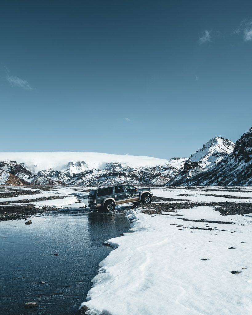 Midgard Adventure super jeep crossing a glacial river in Thorsmork surrounded by snow-covered mountains and Eyjafjallajokull glacier